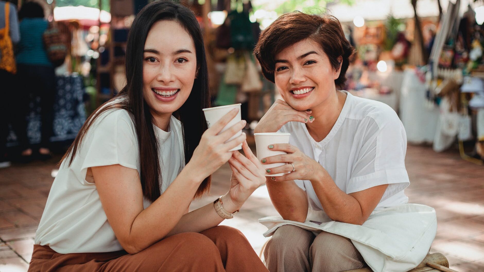 pretty asian women with takeaway coffees sitting in outdoor cafe